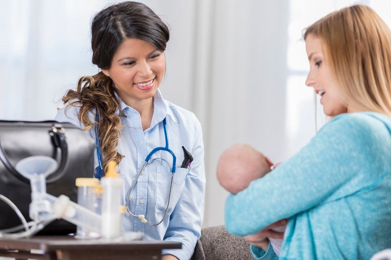 Lactation consultant smiling at a new mom holding her baby.
