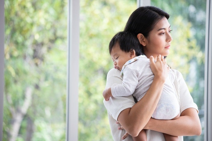 Mom holding her newborn baby and looking out a window.