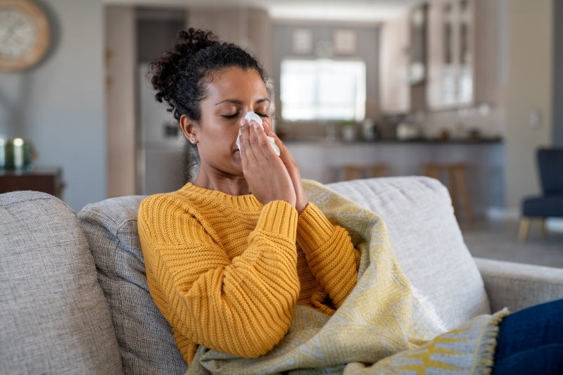 woman on couch blowing her nose