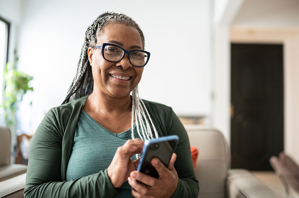A woman wearing braces smiles as she taps her phone screen to contact a doctor