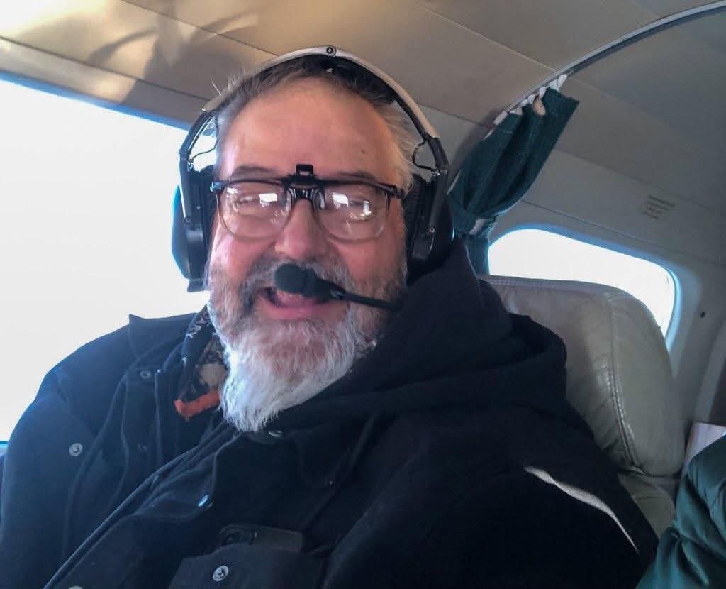 Bruce in airplane wearing headphones and smiling