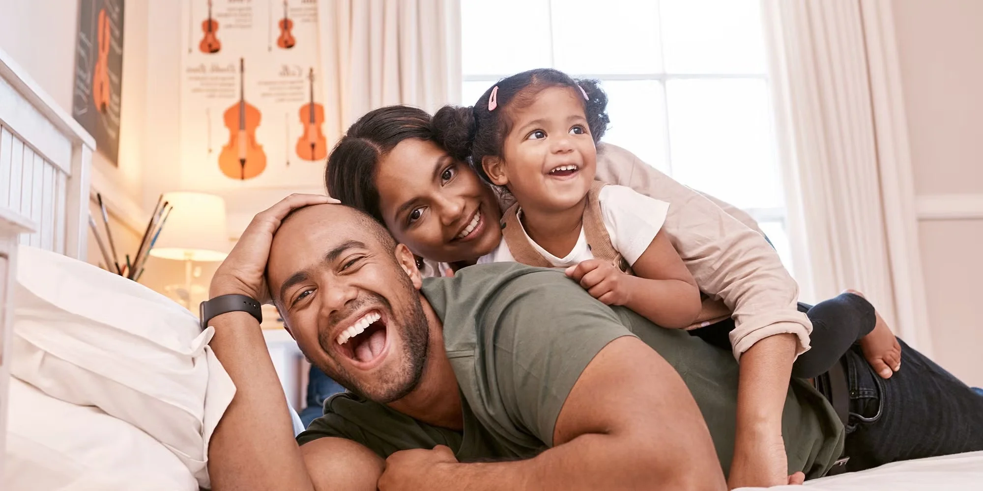 A family of three happily piles on top of each other, laughing, on a bed in their home