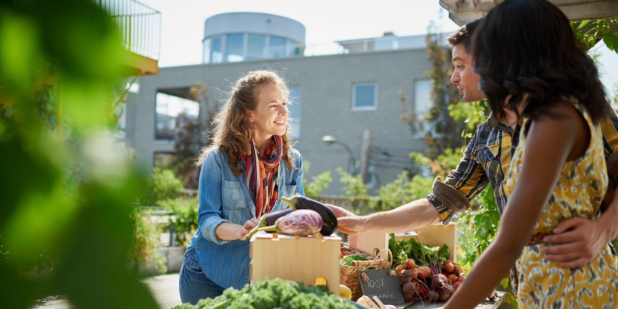 A woman engages in conversation with a couple running a farmer's market stand