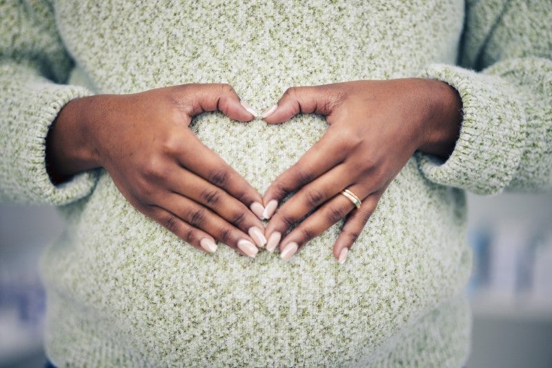 woman in sweater with hands forming a heart over pregnant belly