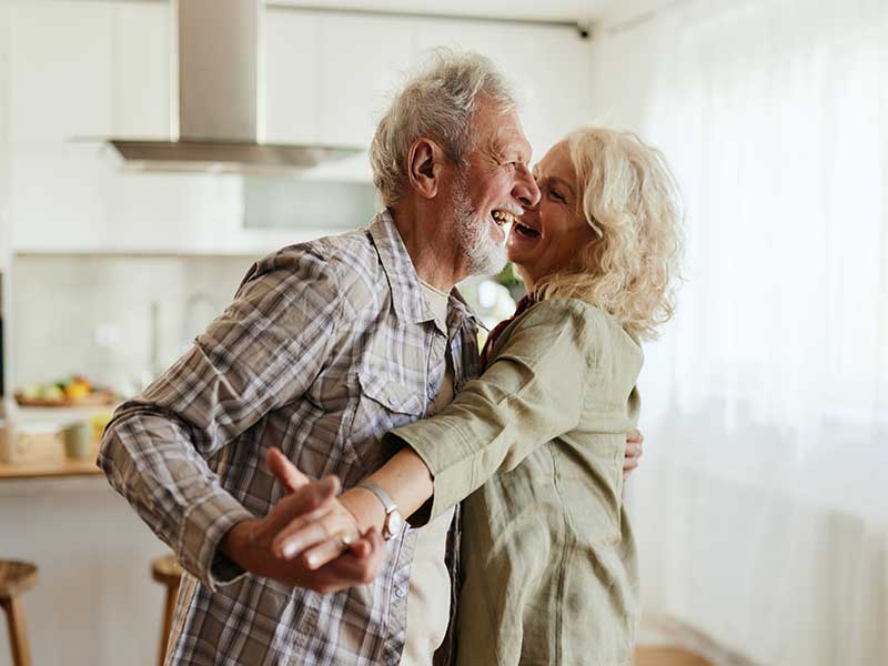 An elderly couple dances joyfully in their kitchen