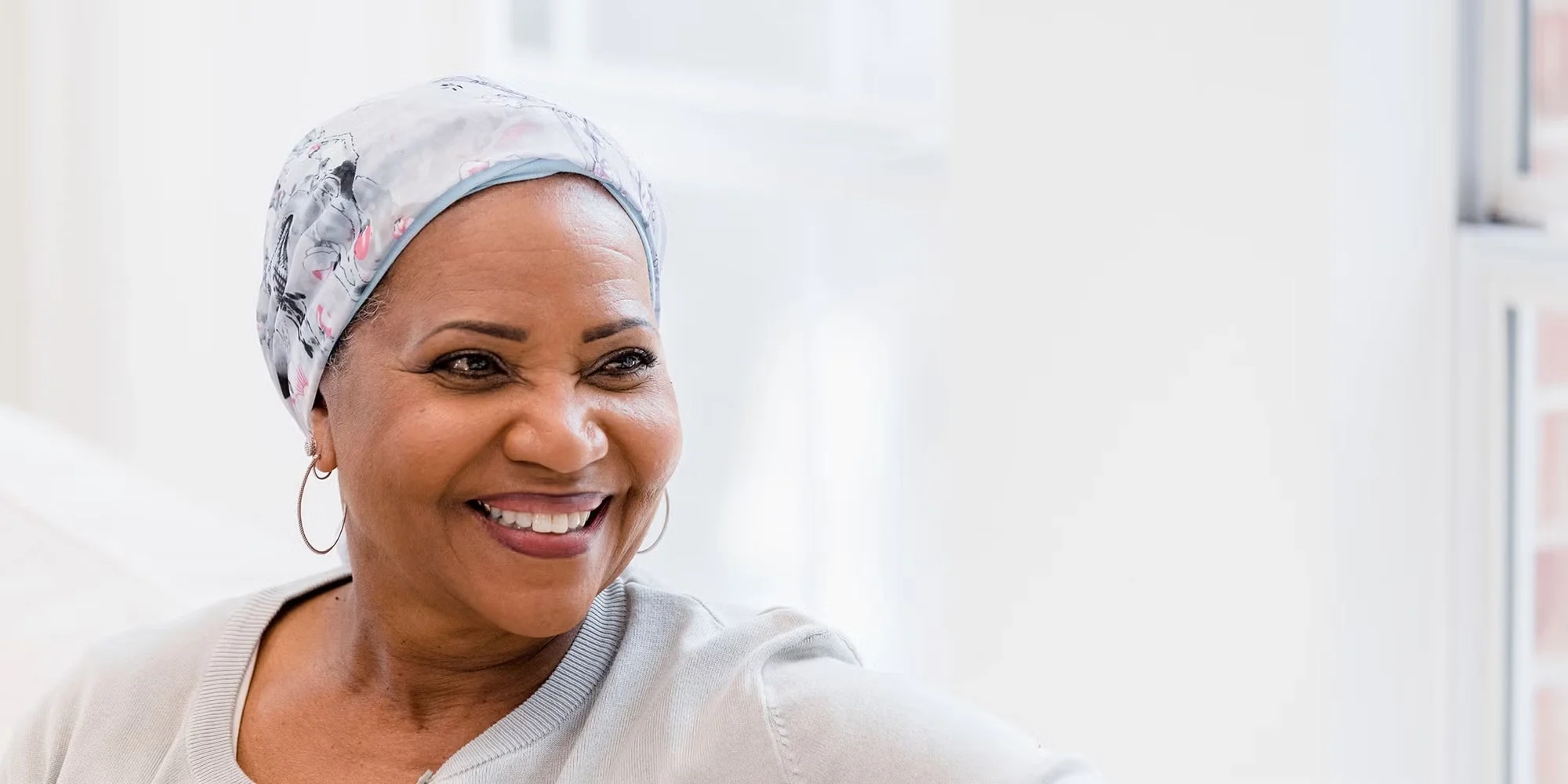 A middle-aged woman smiles off into the distance. She's wearing a scarf on her head as part of her cancer journey.