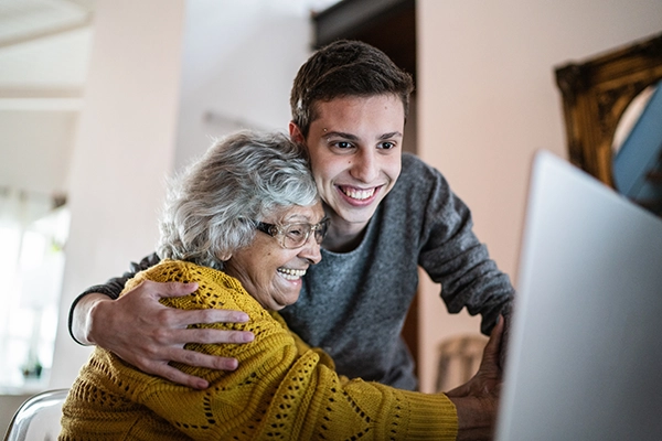 A grandson hugs his grandmother while they look at a laptop screen