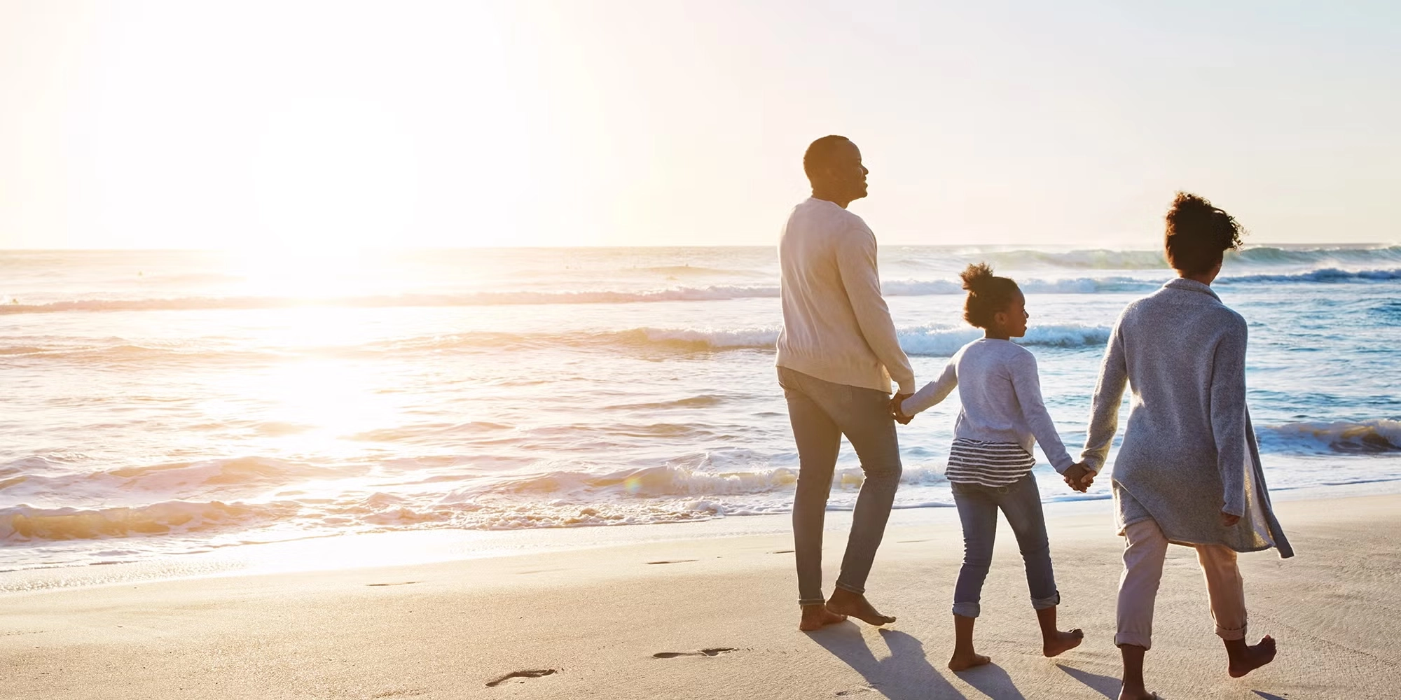 A family of three walks hand in hand together on the beach