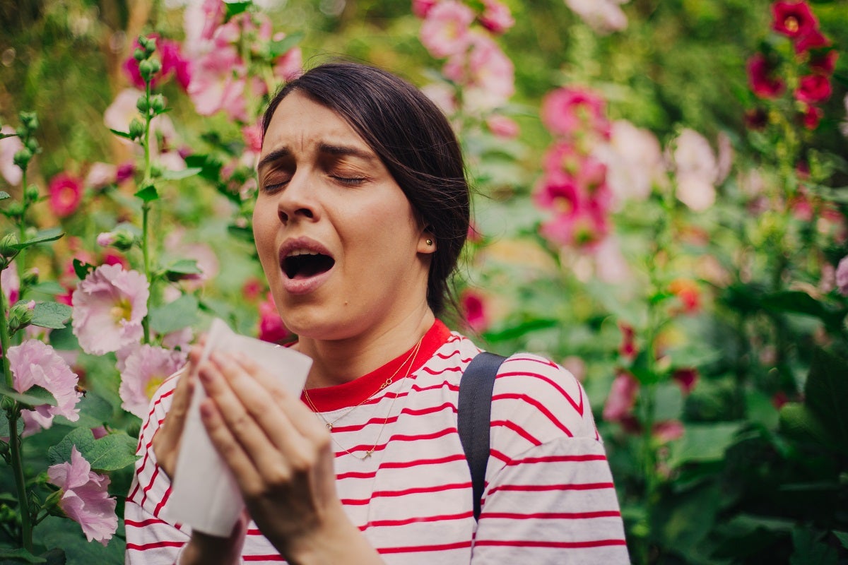 Woman sneezing outside surrounded by pink flowers.