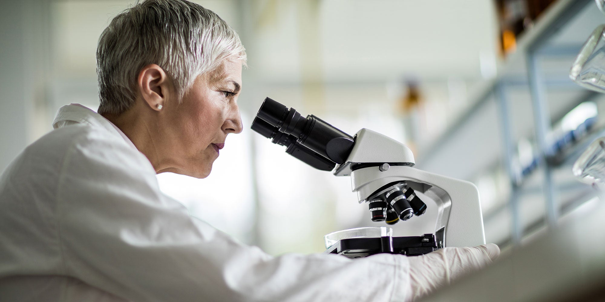 A woman conducts research under a microscope in a lab