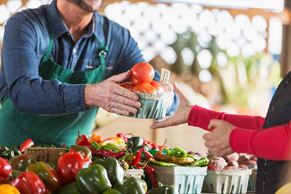 A man hands over a bundle of vegetables at a farmer's market